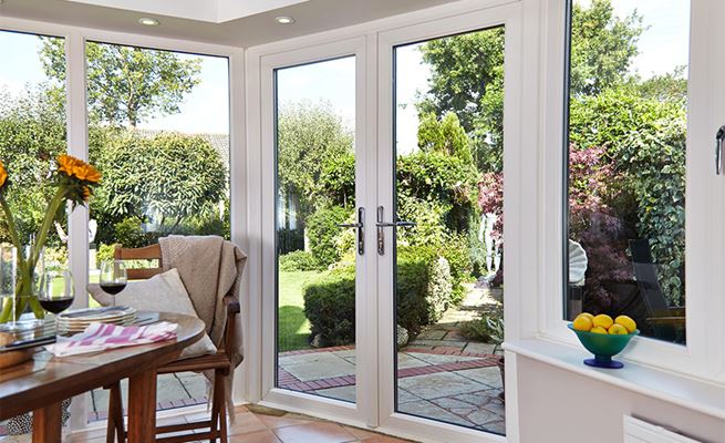 Dual white and anthracite grey uPVC French doors with chrome handles in dining room looking out on garden